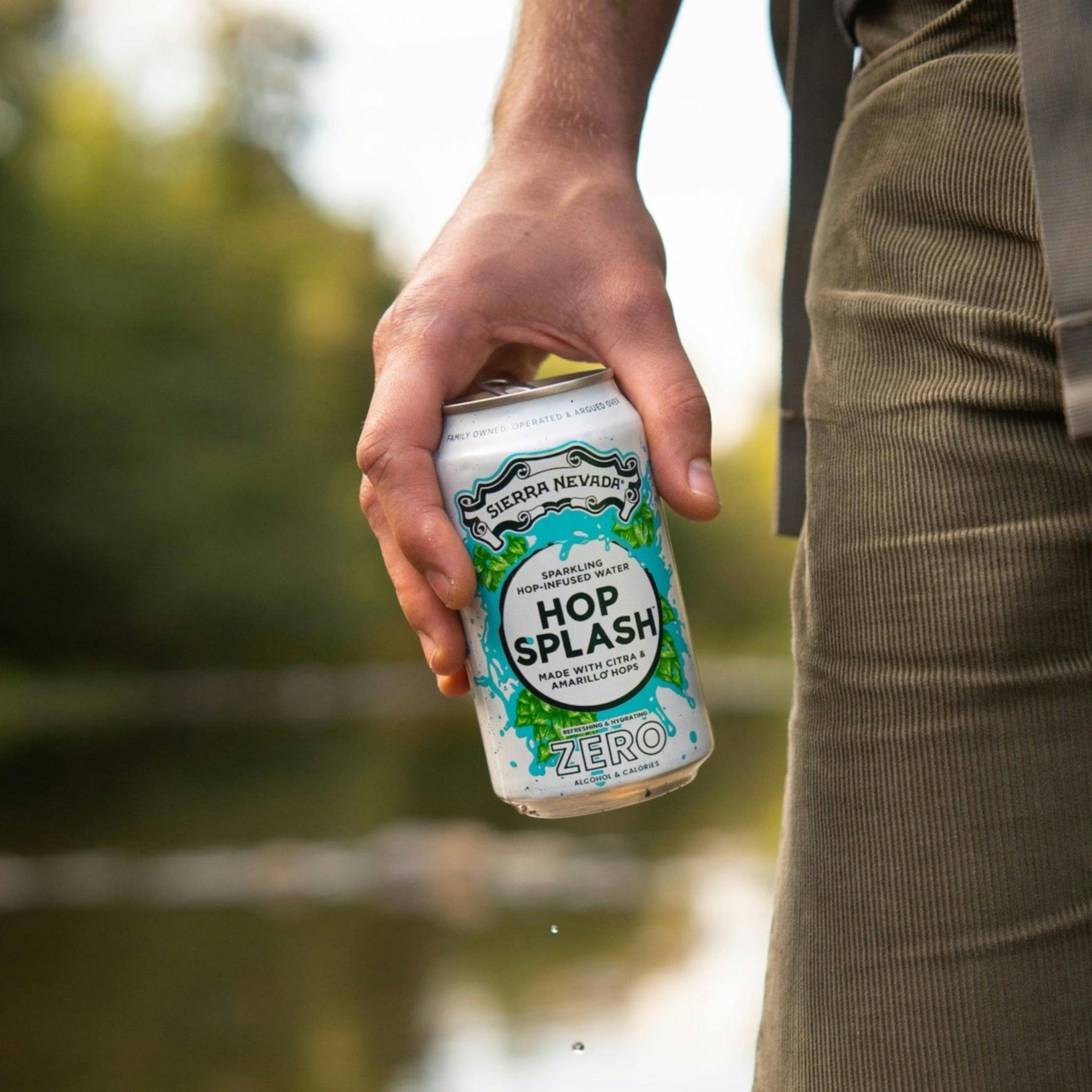 A hiker holding a can of Sierra Nevada Hop Splash on the bank of a river