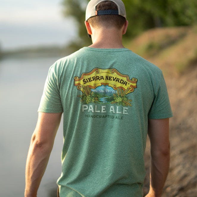 A man walks along a peaceful river wearing the Sierra Nevada Brewing Co. Pale Ale t-shirt, as viewed from behind.
