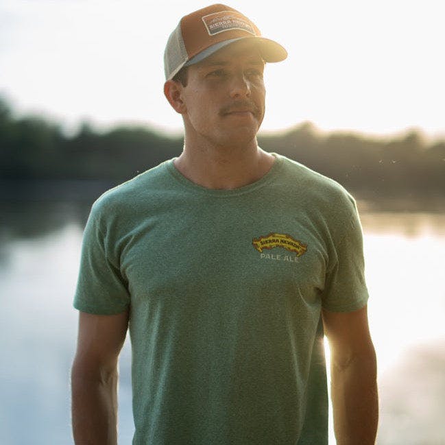 A man wears the Sierra Nevada Pale Ale T-Shirt while standing alongside a river.