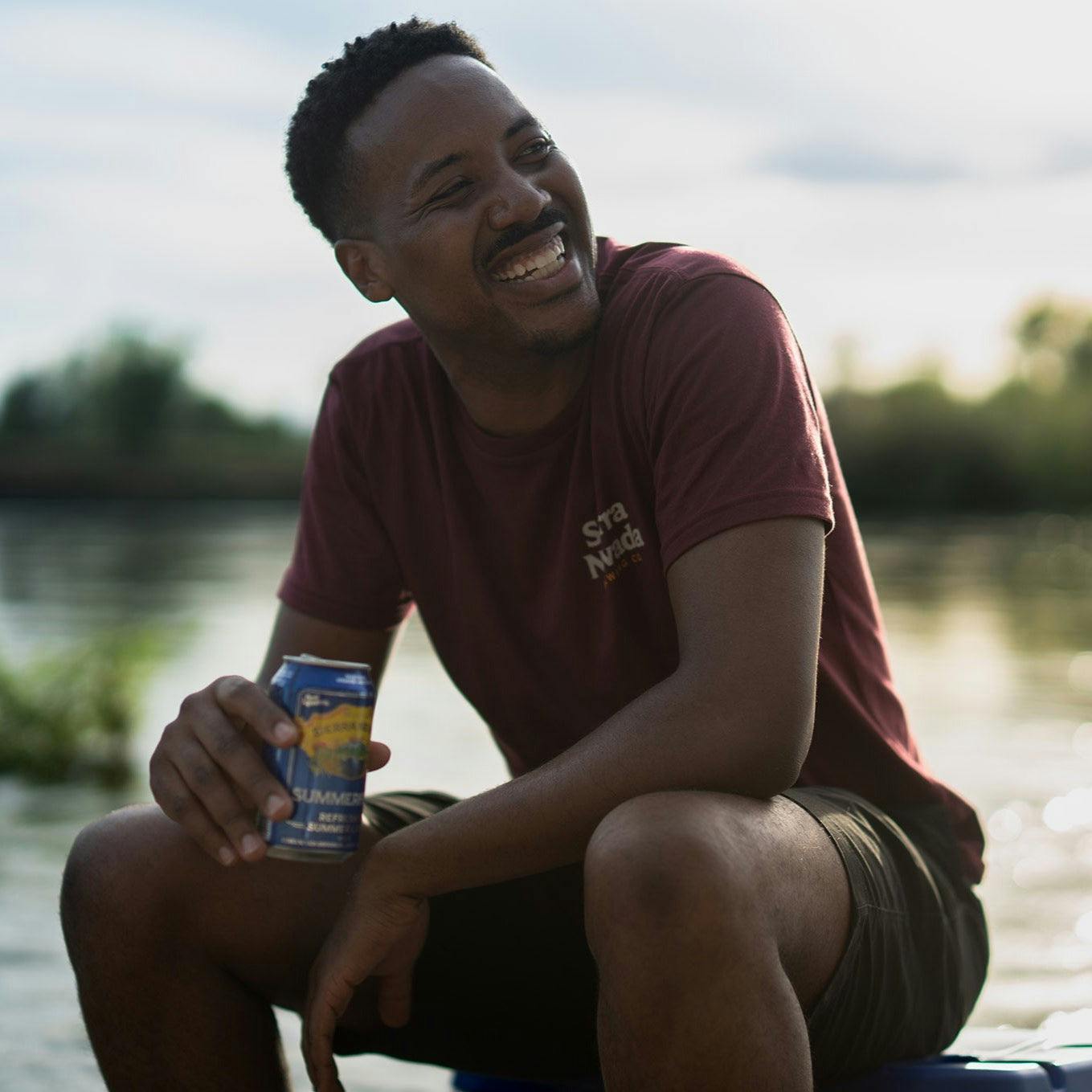 Sierra Nevada Brewing Co. Trail T-Shirt worn by a man sitting on a cooler by a river enjoying a Summerfest beer.