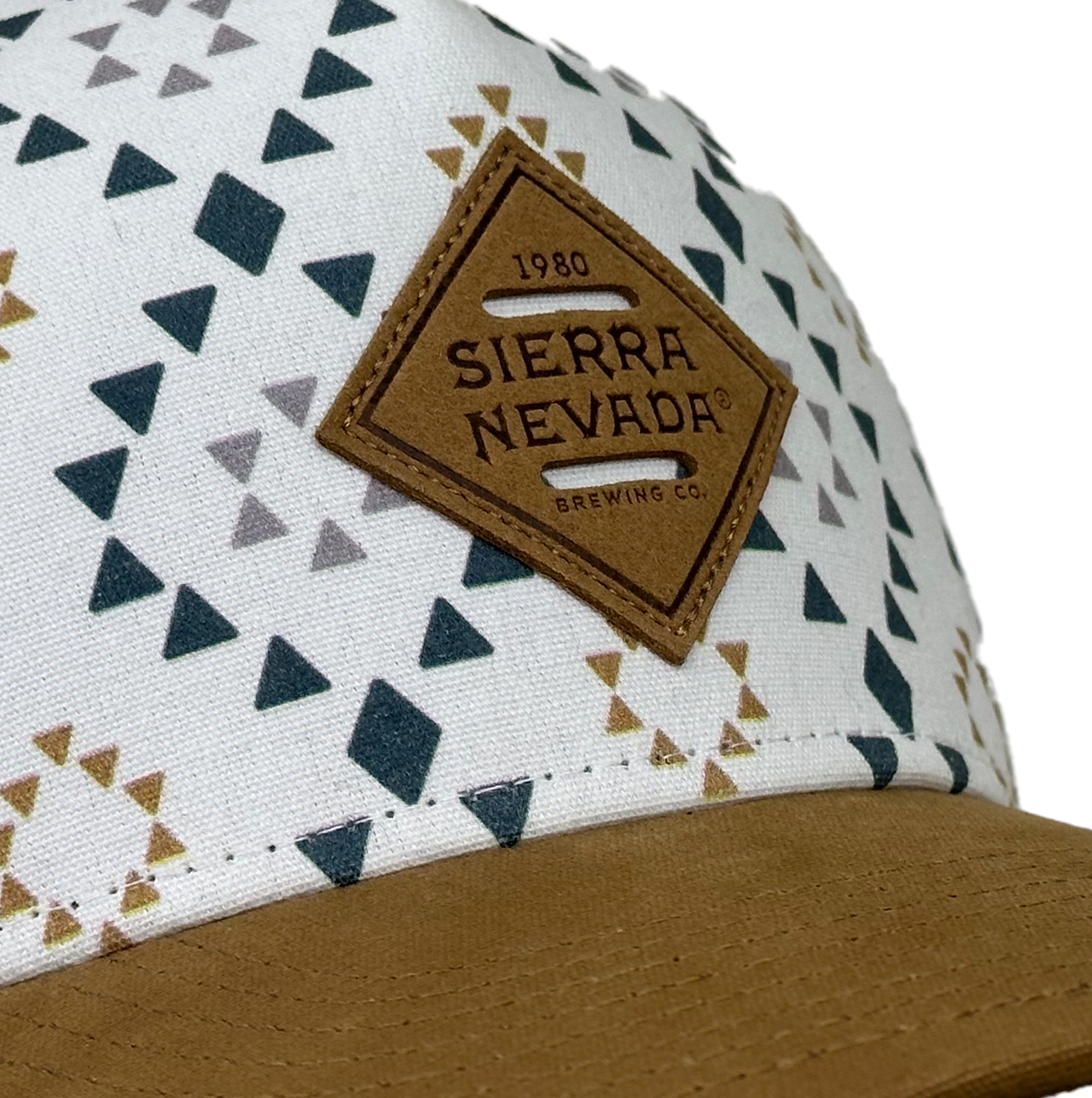 Sierra Nevada Brewing Co. Hop Spring Trucker Hat - close up view of the leather Sierra Nevada patch on the front of the hat and geometric print background
