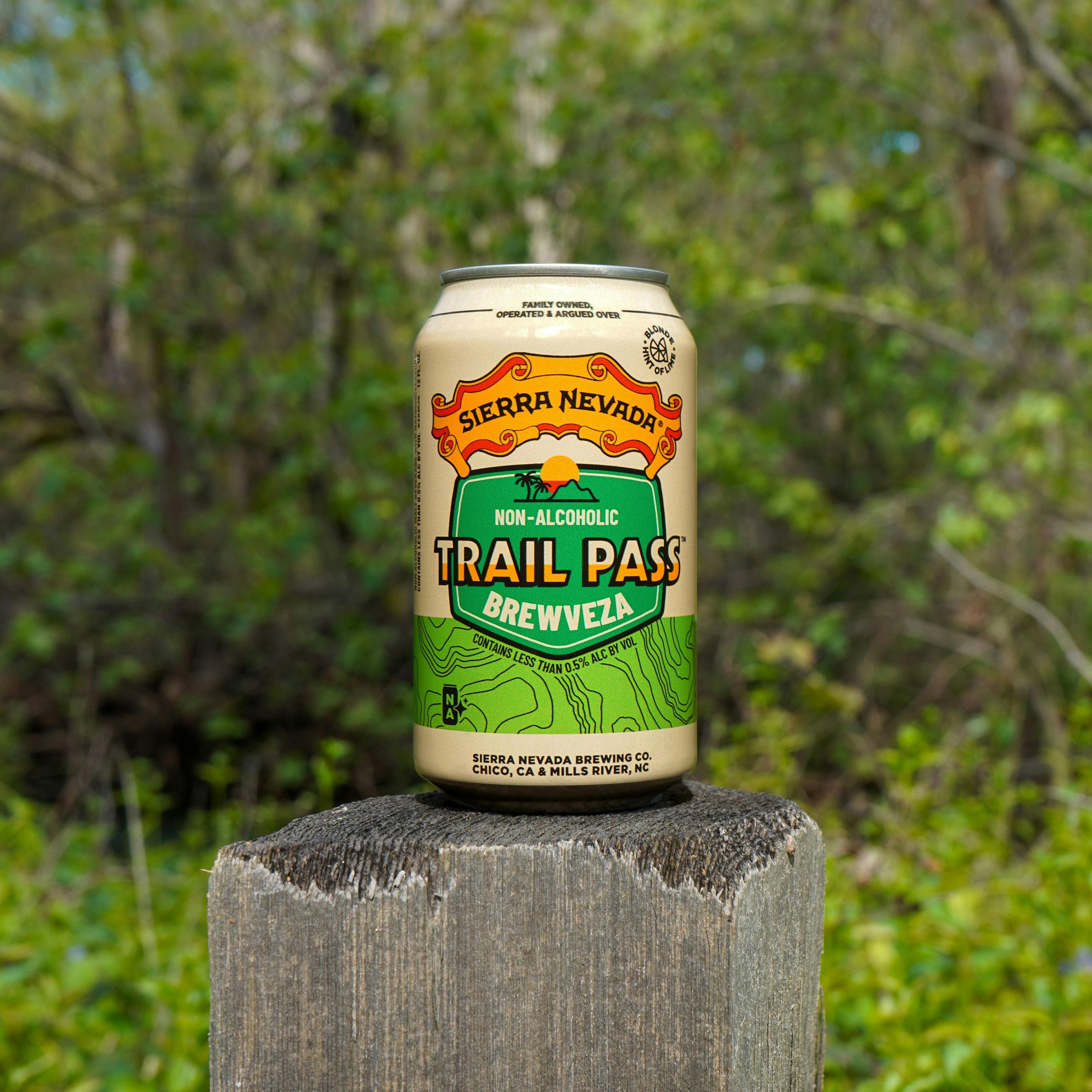Sierra Nevada Trail Pass Brewveza can perched on top of a wooden fence post in front of a wooded area