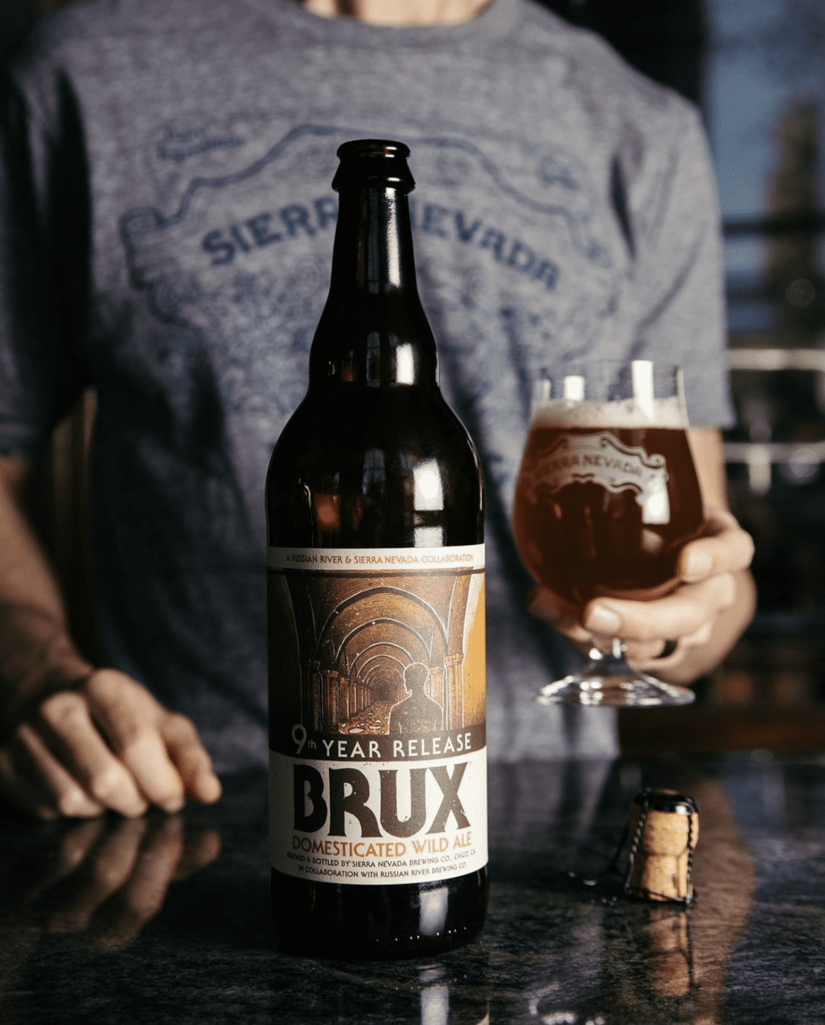 A bottle of Brux sits on a bar in front of a man, alongside a freshly poured pint